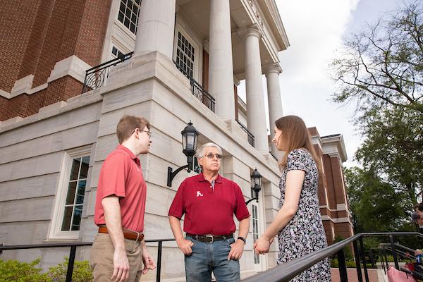 Two students and a professor talk outside an academic hall